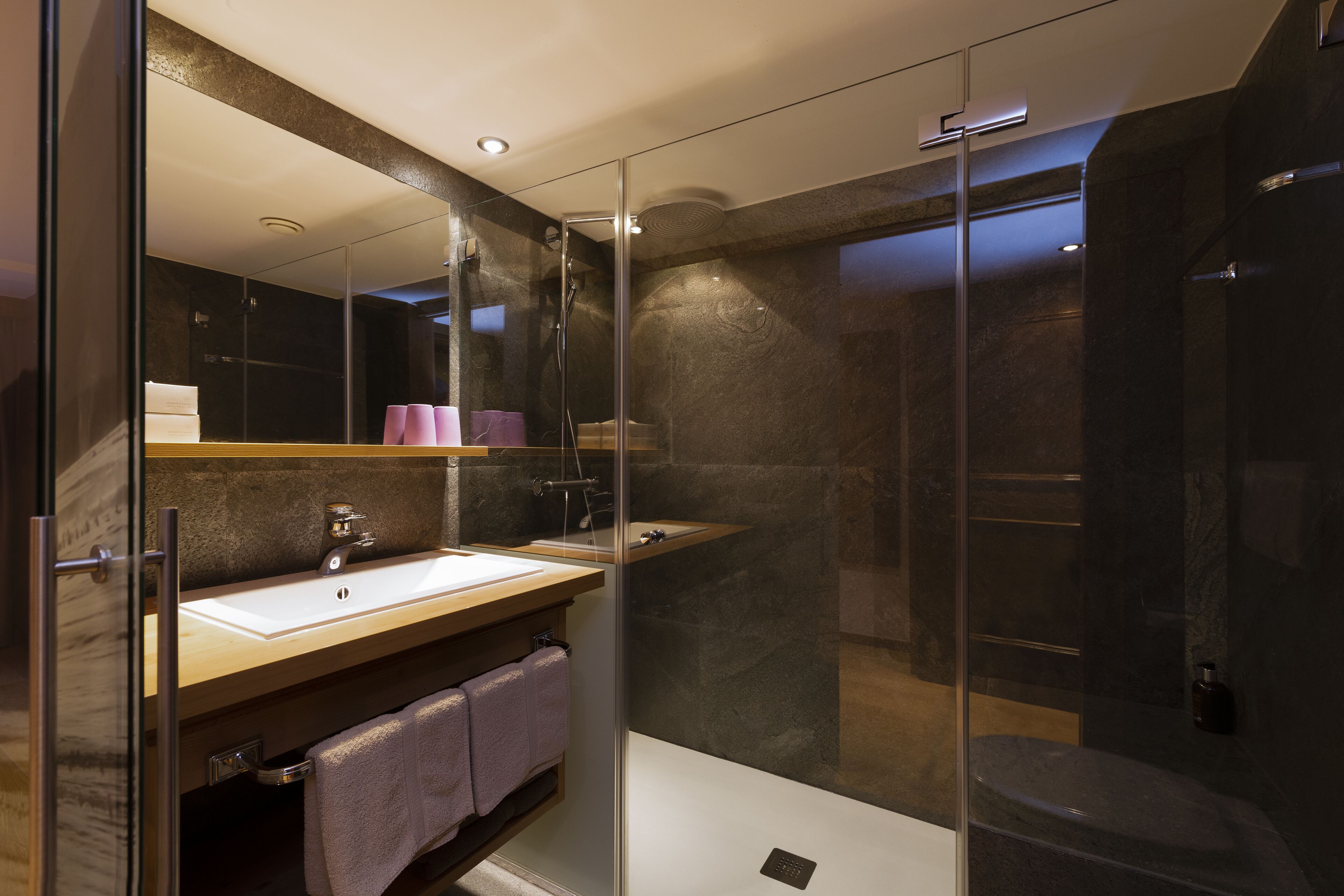 Un baño moderno con ducha de vidrio, lavamanos con encimera de mármol y un espejo grande.