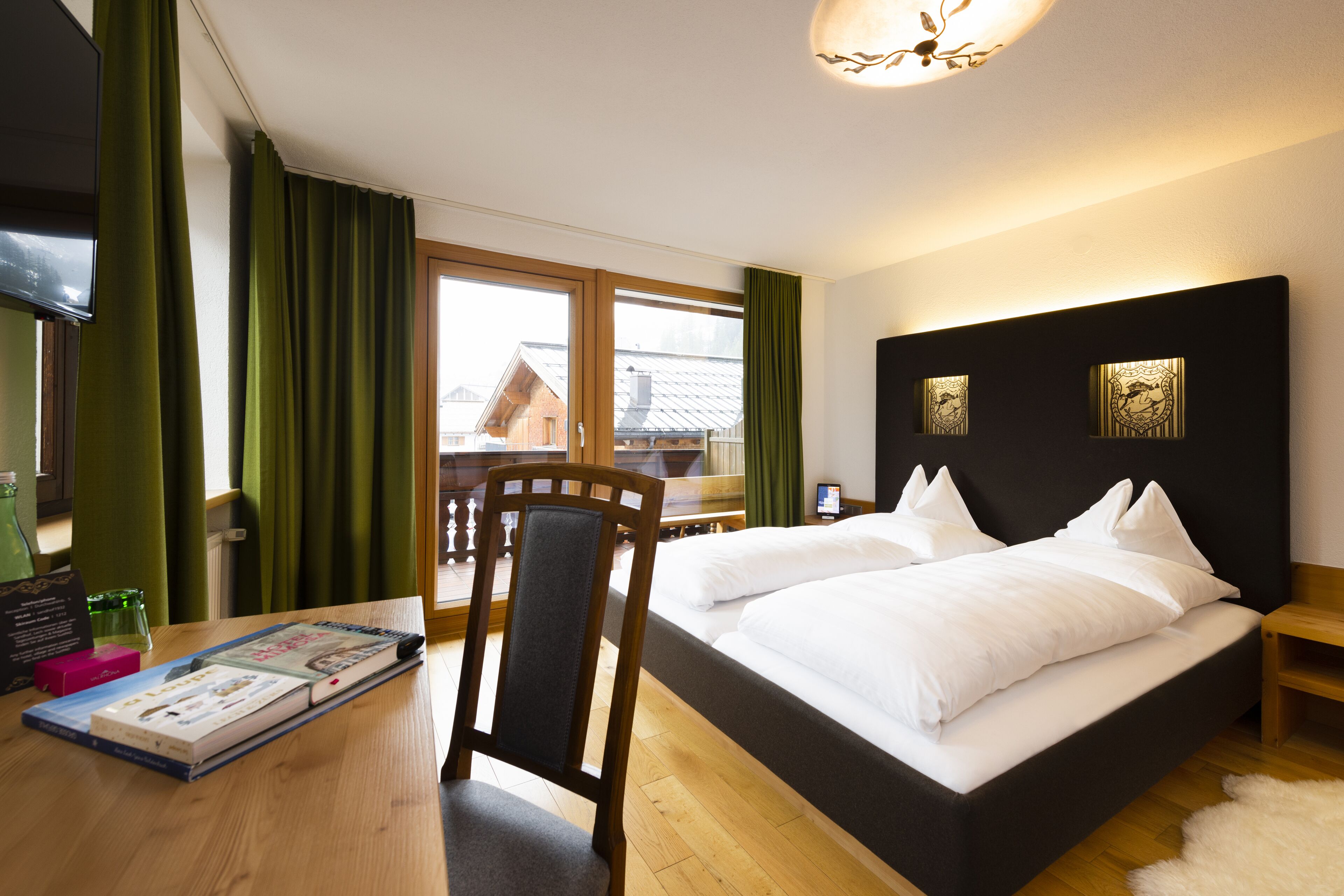 A hotel room with a bed, a desk with books, a chair, and a TV.