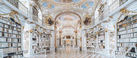 A grand library with ornate ceilings, extensive bookcases, and a checkered floor.
