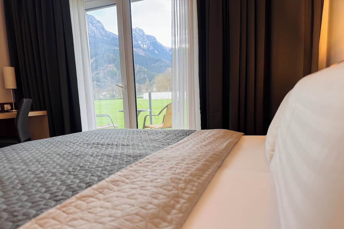 A hotel room with a bed, a desk, and a view of mountains through the window.