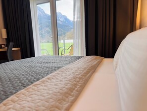 A hotel room with a bed, a desk, and a view of mountains through the window. - Hotel Spirodom Admont (Admont)