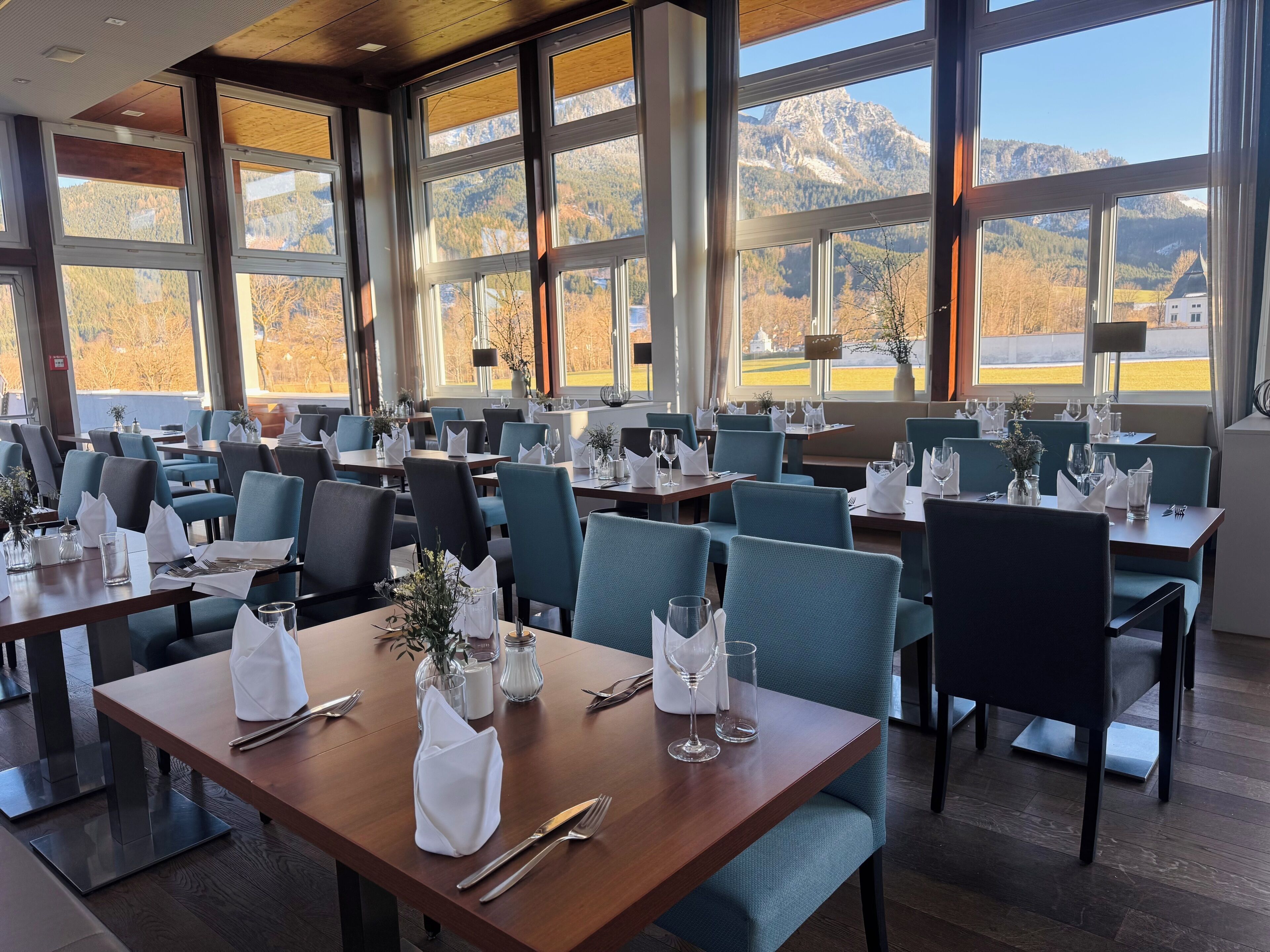 Un restaurante con varias mesas y sillas, amplias ventanas que ofrecen vistas a la montaña y un interior moderno y limpio.