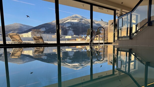 A modern indoor swimming pool with a glass floor, reflecting the surrounding buildings and mountains. - Hotel Spirodom Admont (Admont)