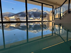 A modern indoor swimming pool with a glass floor, reflecting the surrounding buildings and mountains. - Hotel Spirodom Admont (Admont)