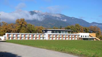 A modern building with a flat roof and large windows, surrounded by a grassy field and trees with autumn foliage.