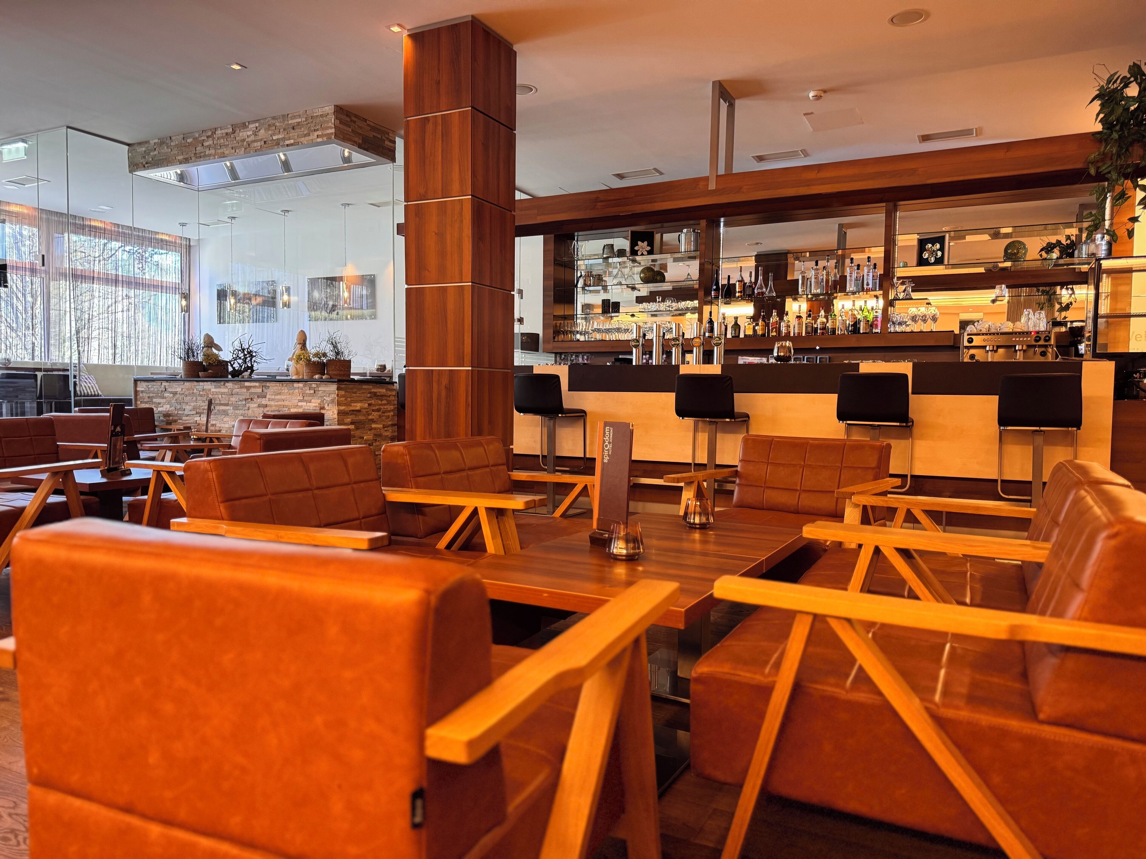 A modern bar area with leather seating, a wooden column, and a bar stocked with bottles and glasses.