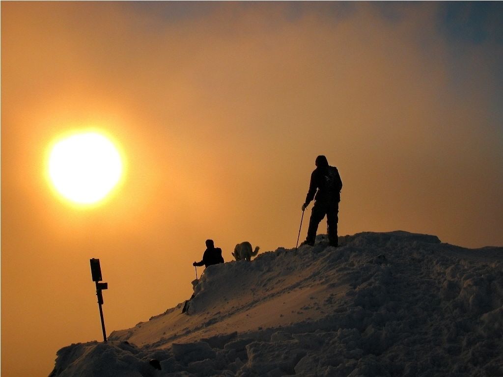 A silhouette of a person on a snowy hill with a sun in the background.