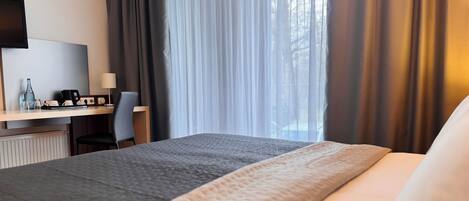 Habitación de hotel con cama, escritorio, silla, televisor y ventana con cortinas.