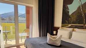 A hotel room with a bed, a chair, a table, and a view of a mountain and buildings through a glass door. - Hotel Spirodom Admont (Admont)