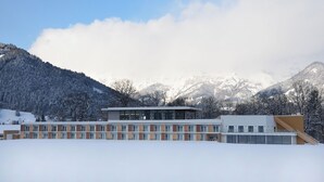 A modern building with a flat roof and large windows, surrounded by snow-covered mountains. - Hotel Spirodom Admont (Admont)