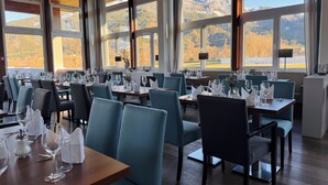 Ein Restaurant mit großen Fenstern und Blick auf die Berge, ordentlich angerichteten Tischen mit Stühlen und einem modernen Innenraum.