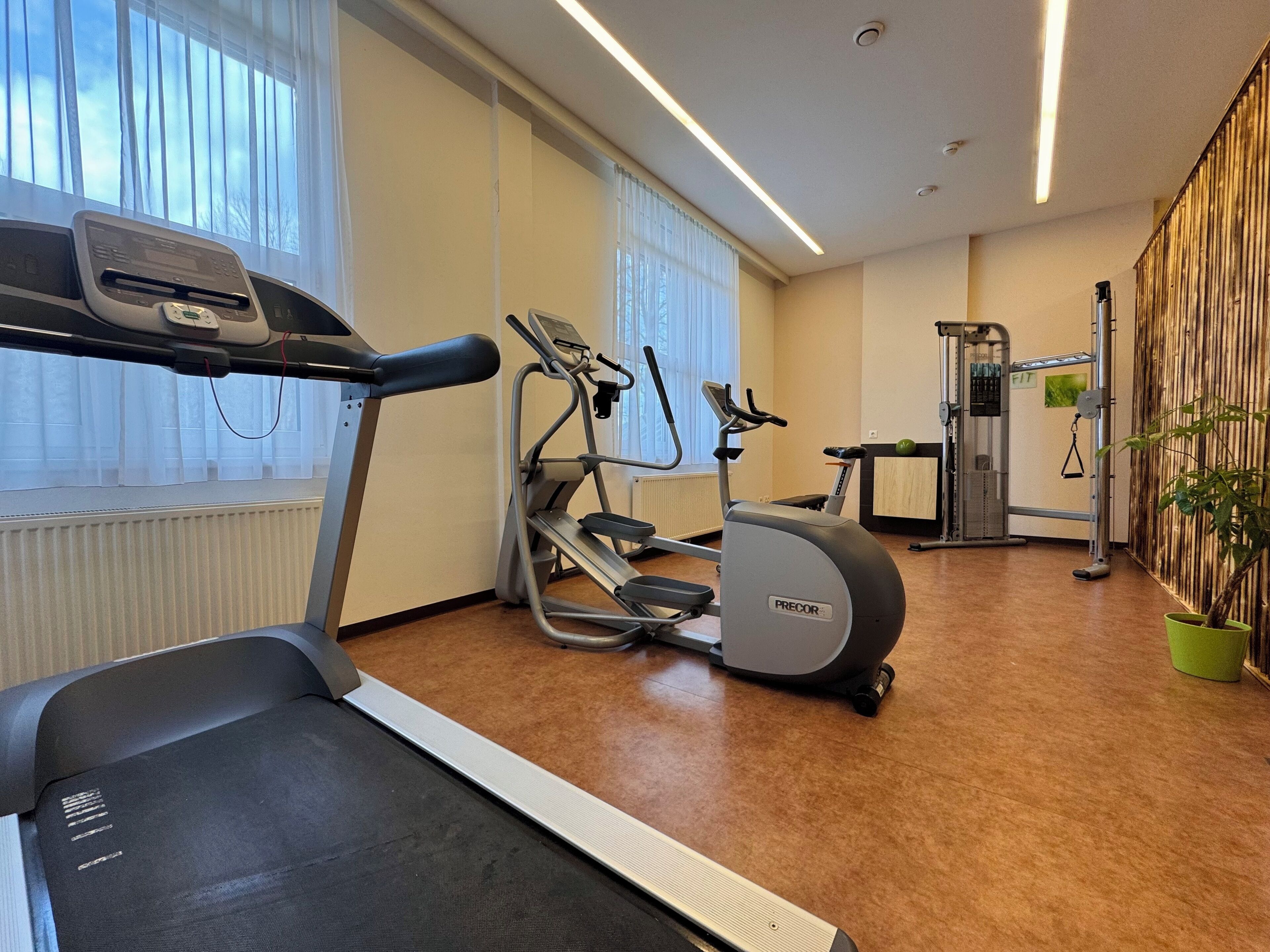 Een fitnessruimte met een loopband, elliptische trainer en krachttrainingapparaat.
