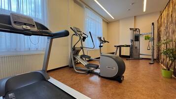 Een fitnessruimte met een loopband, elliptische trainer en krachttrainingapparaat.