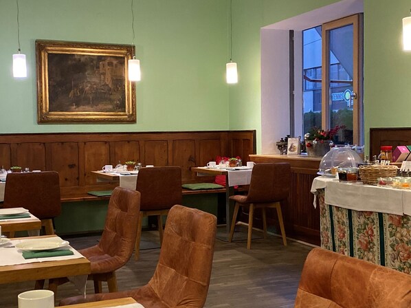 A dining area with wooden booths and tables, a painting on the wall, and a window with a view of the outside. - Bergland Hotel (Salzburg)