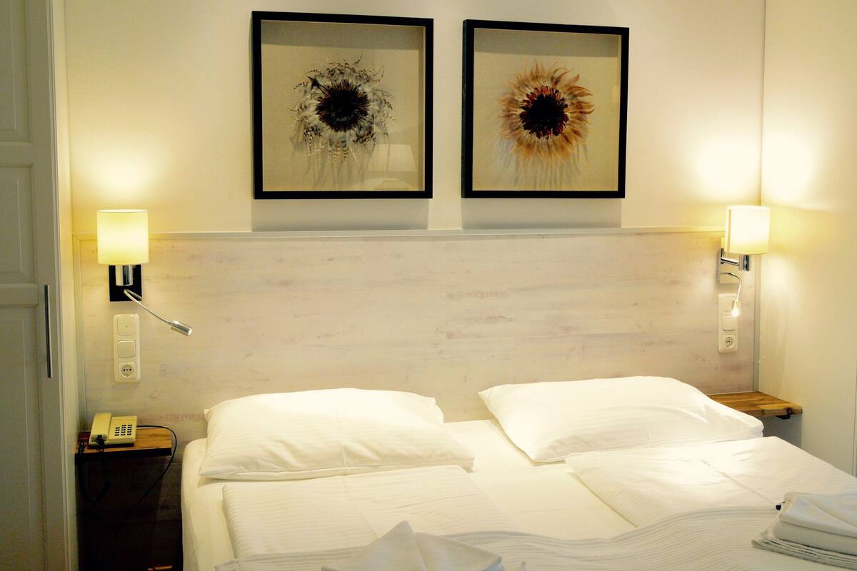 Ein Hotelzimmer mit einem Doppelbett, zwei Wandlampen und zwei gerahmten floralen Kunstwerken über dem Bett.