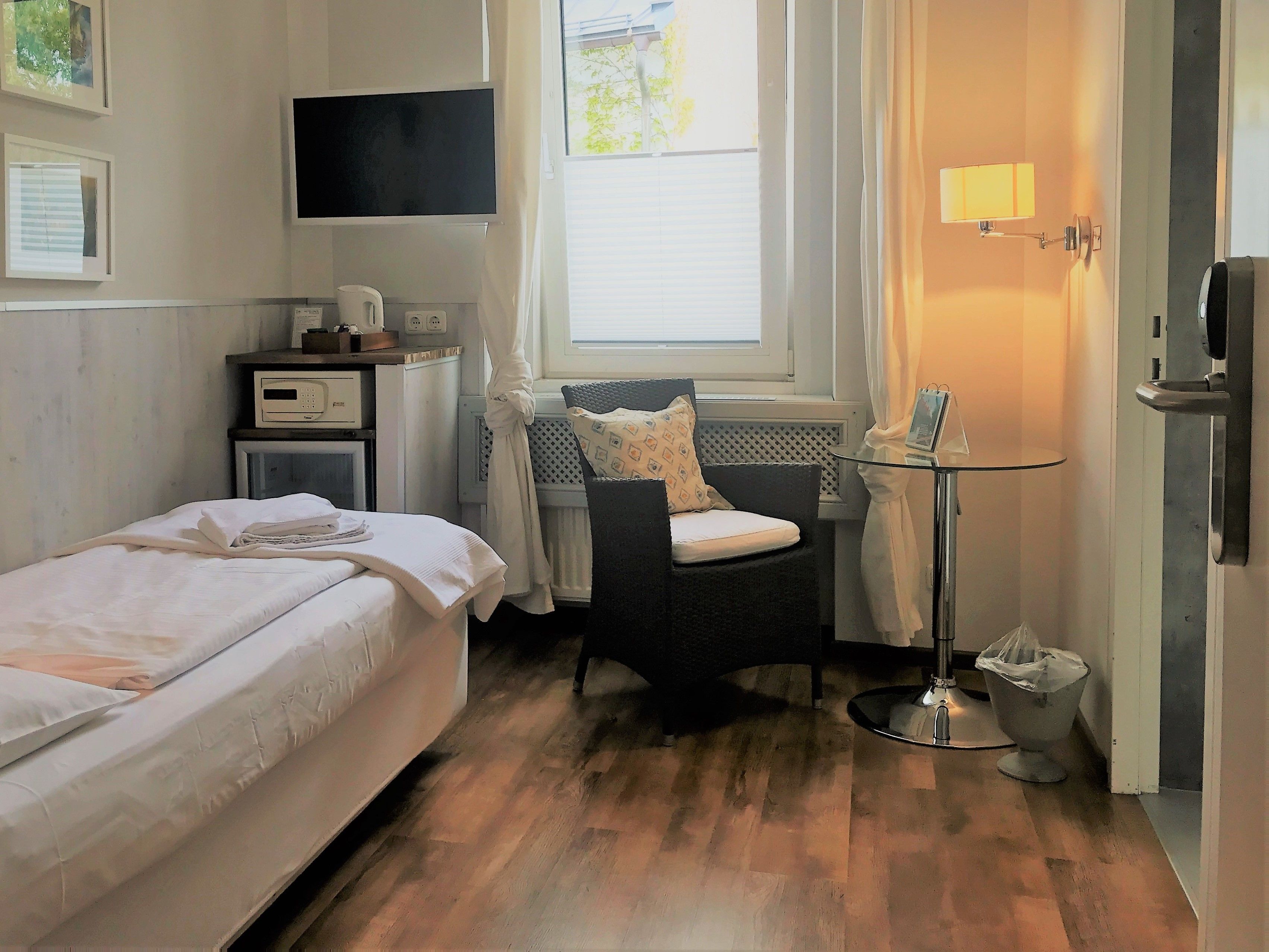 Une chambre d’hôtel avec un lit, une chaise, une petite table, un téléviseur et une fenêtre avec des rideaux.
