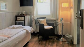 Une chambre d’hôtel avec un lit, une chaise, une petite table, un téléviseur et une fenêtre avec des rideaux.