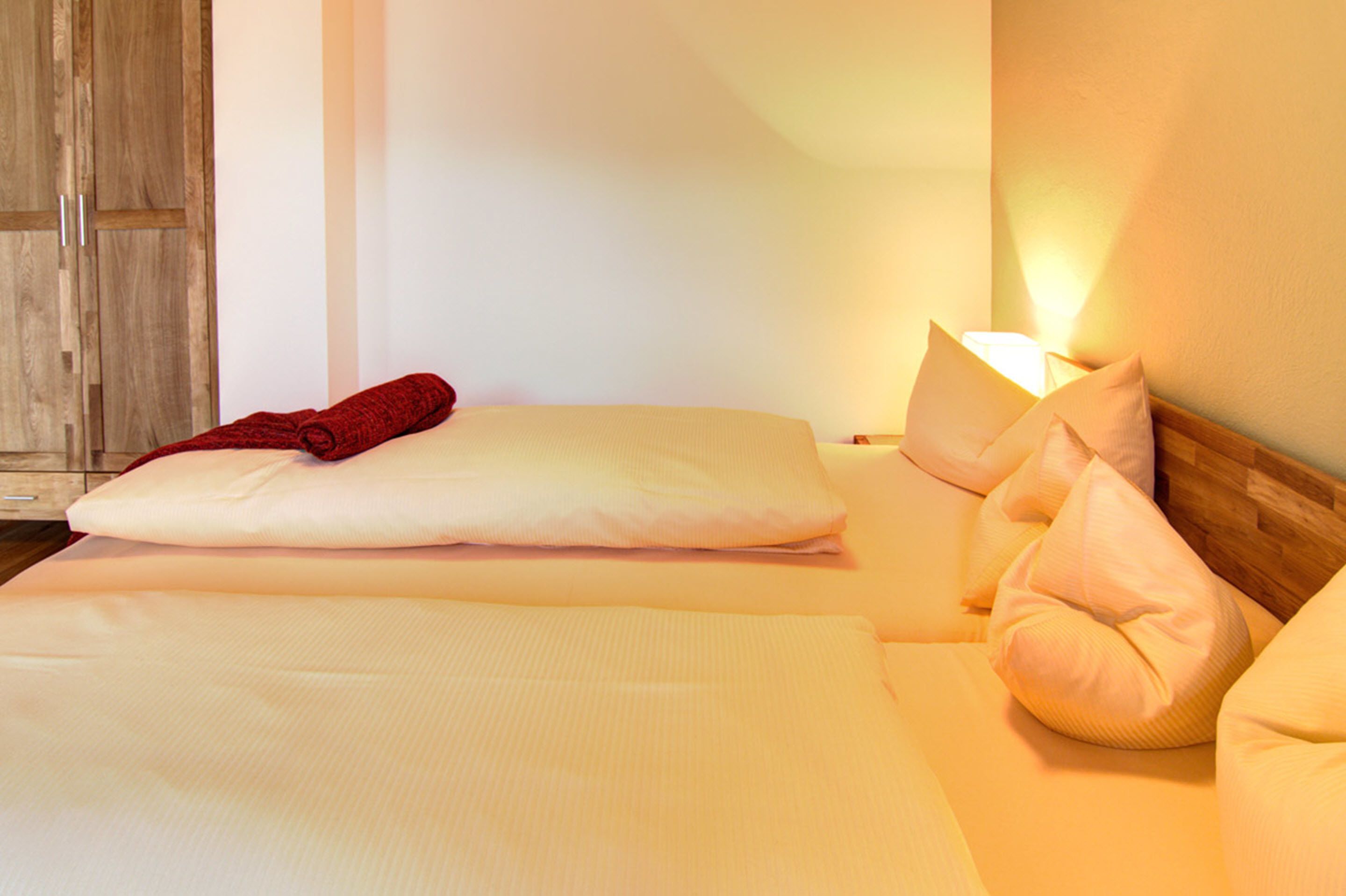 A hotel room with a neatly made bed, a wooden wardrobe, and a bedside lamp.