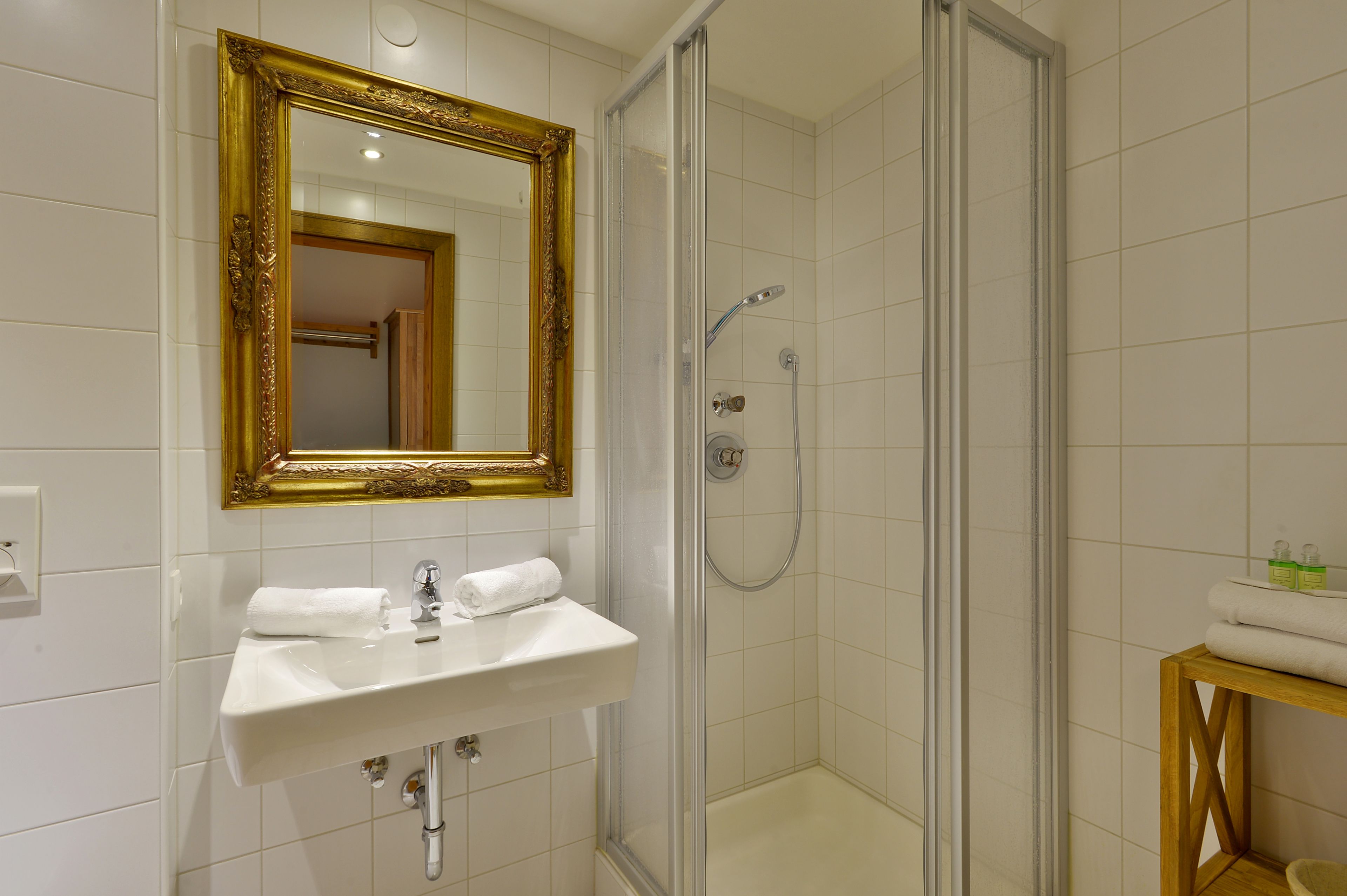 Une salle de bain avec un lavabo blanc, un miroir encadré d’or et une douche fermée par des parois de verre.