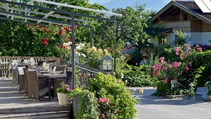 Ulkoterassi, jossa on rottinkihuonekaluja ja pergola, jonka katosta roikkuu kukkia.