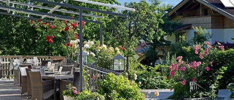 An outdoor seating area with wicker furniture and a pergola with hanging flowers.
