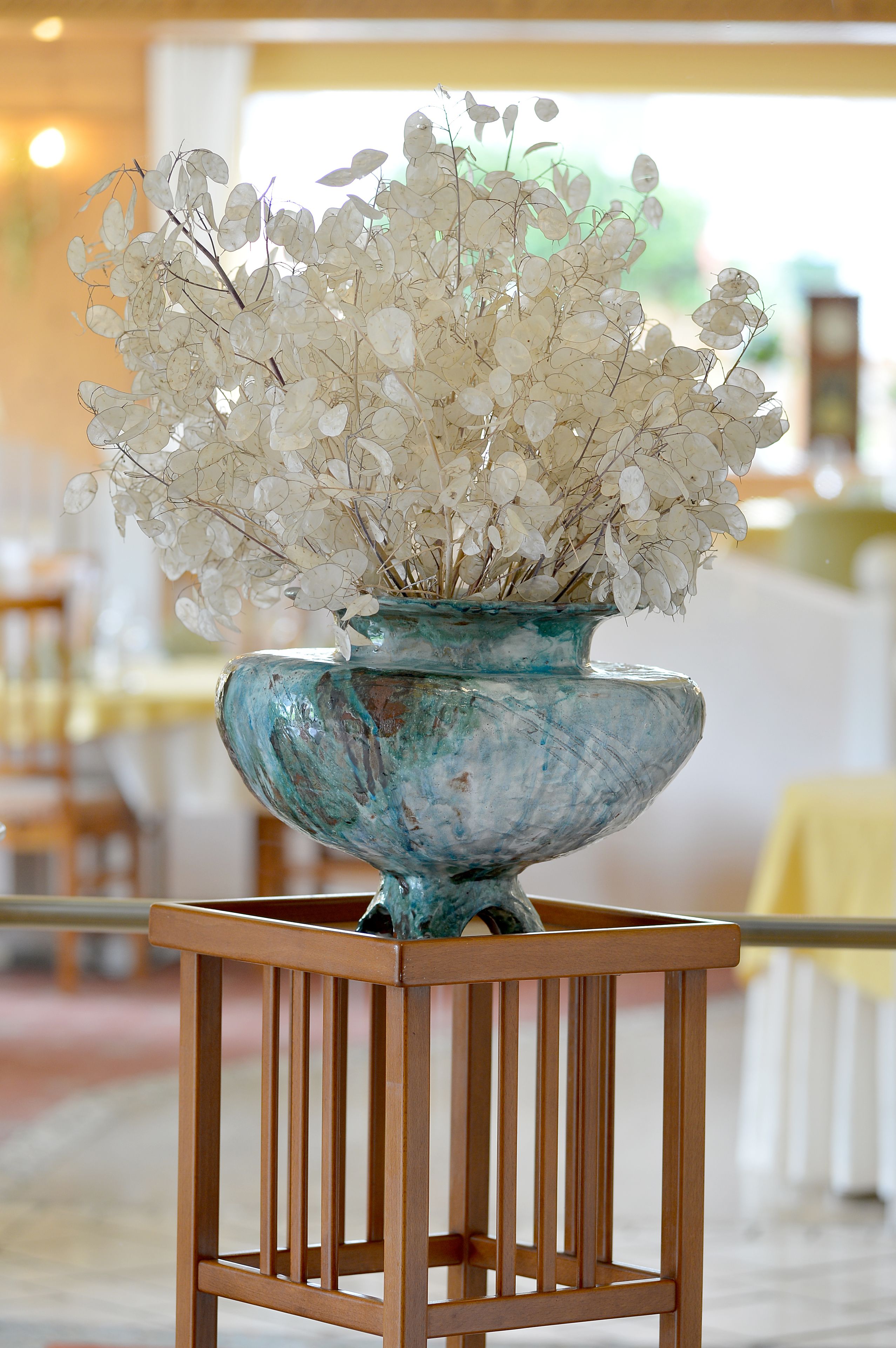 A decorative vase with white flowers on a wooden stand in a well-lit indoor space.