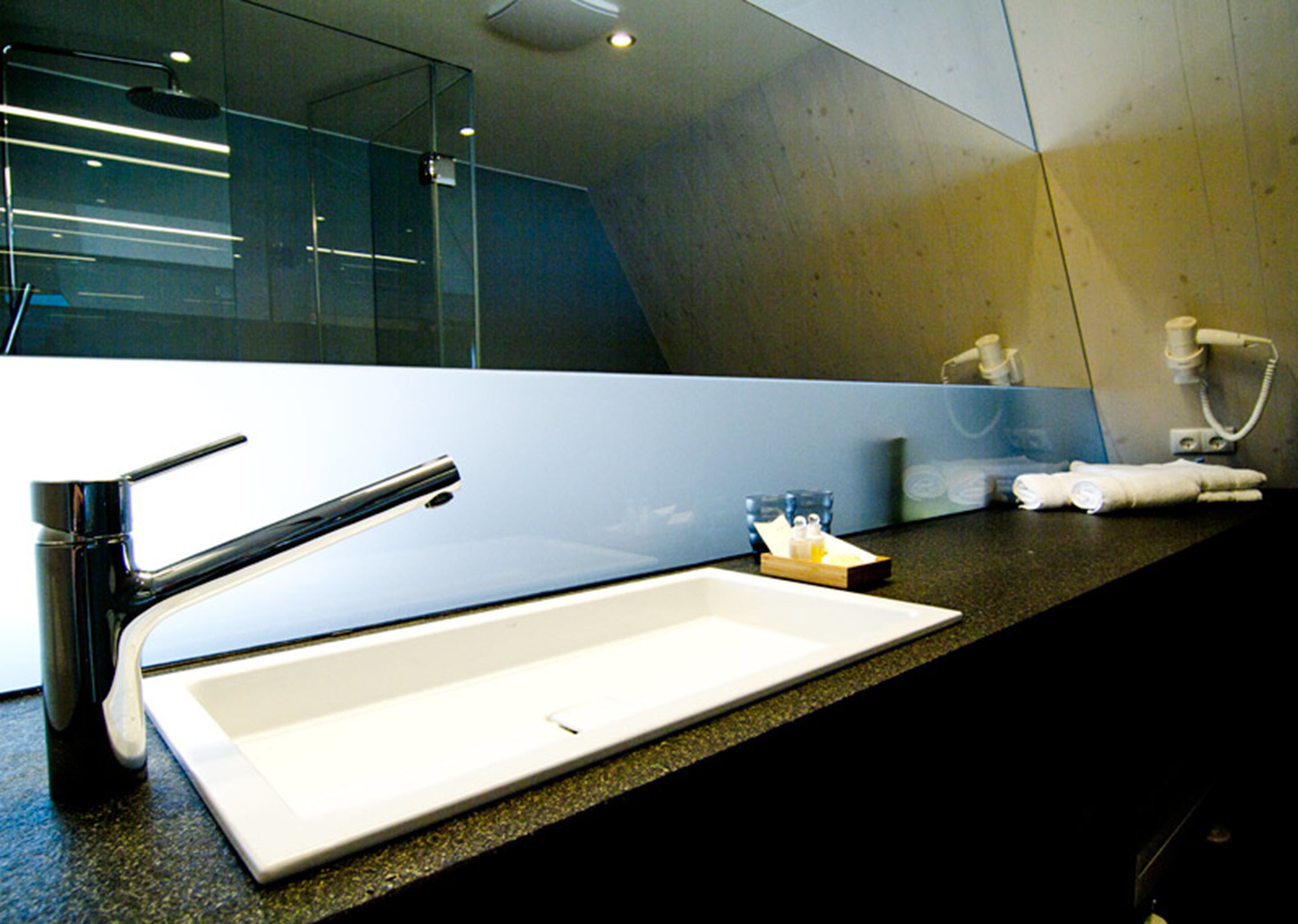 A modern bathroom with a large mirror, a chrome faucet, a white sink, and a towel rack.