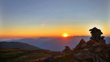 A sunset over a mountainous landscape with a stack of rocks in the foreground.