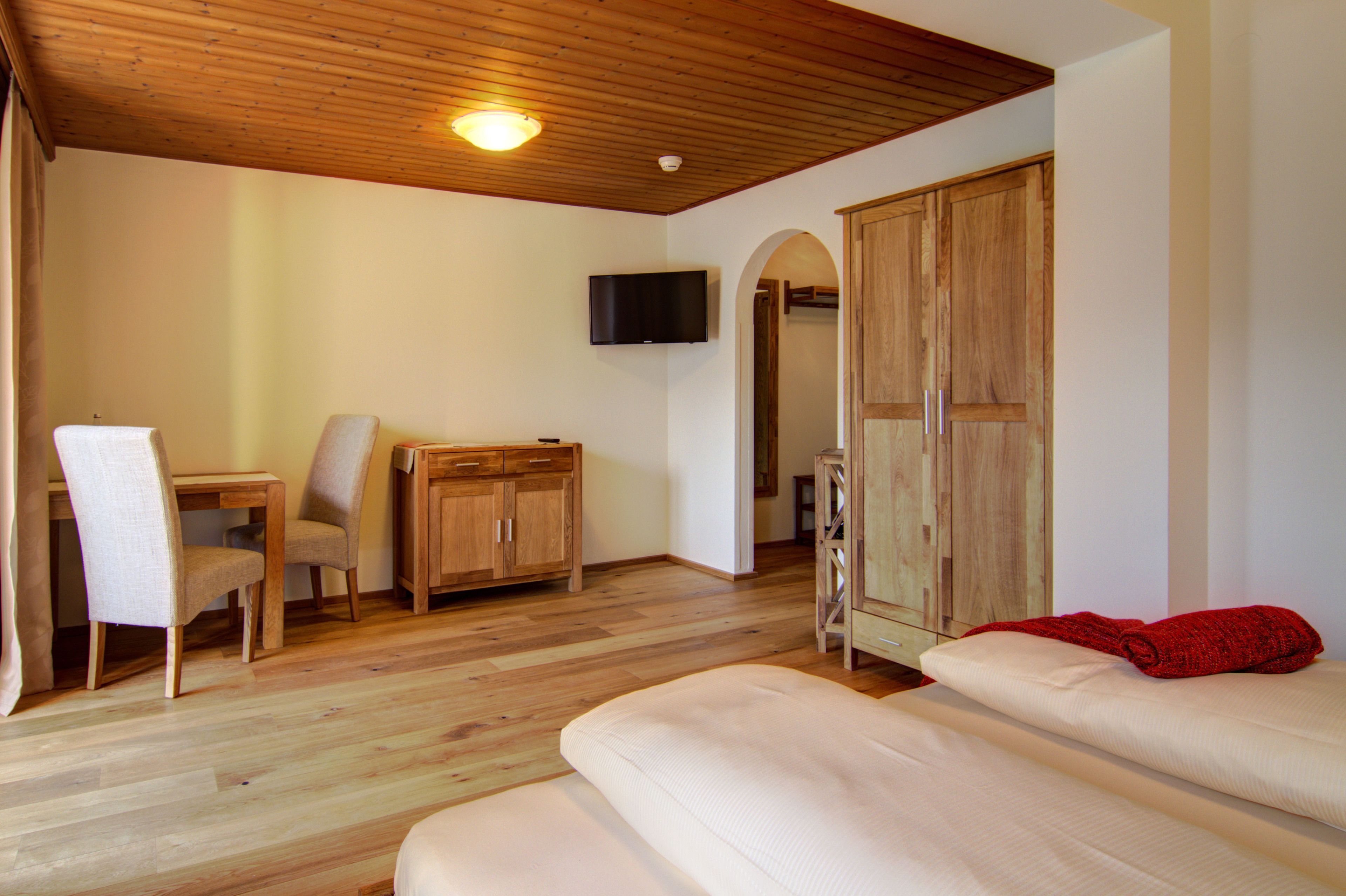 Una habitación con suelo de madera, un sofá, un televisor montado en la pared, un armario de madera y una puerta con espejo.