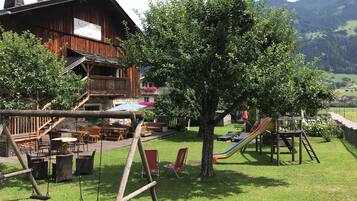 Overlooking lush gardens with a swing set and seating areas, this mountain lodge offers a serene escape with a balcony view of rolling hills.