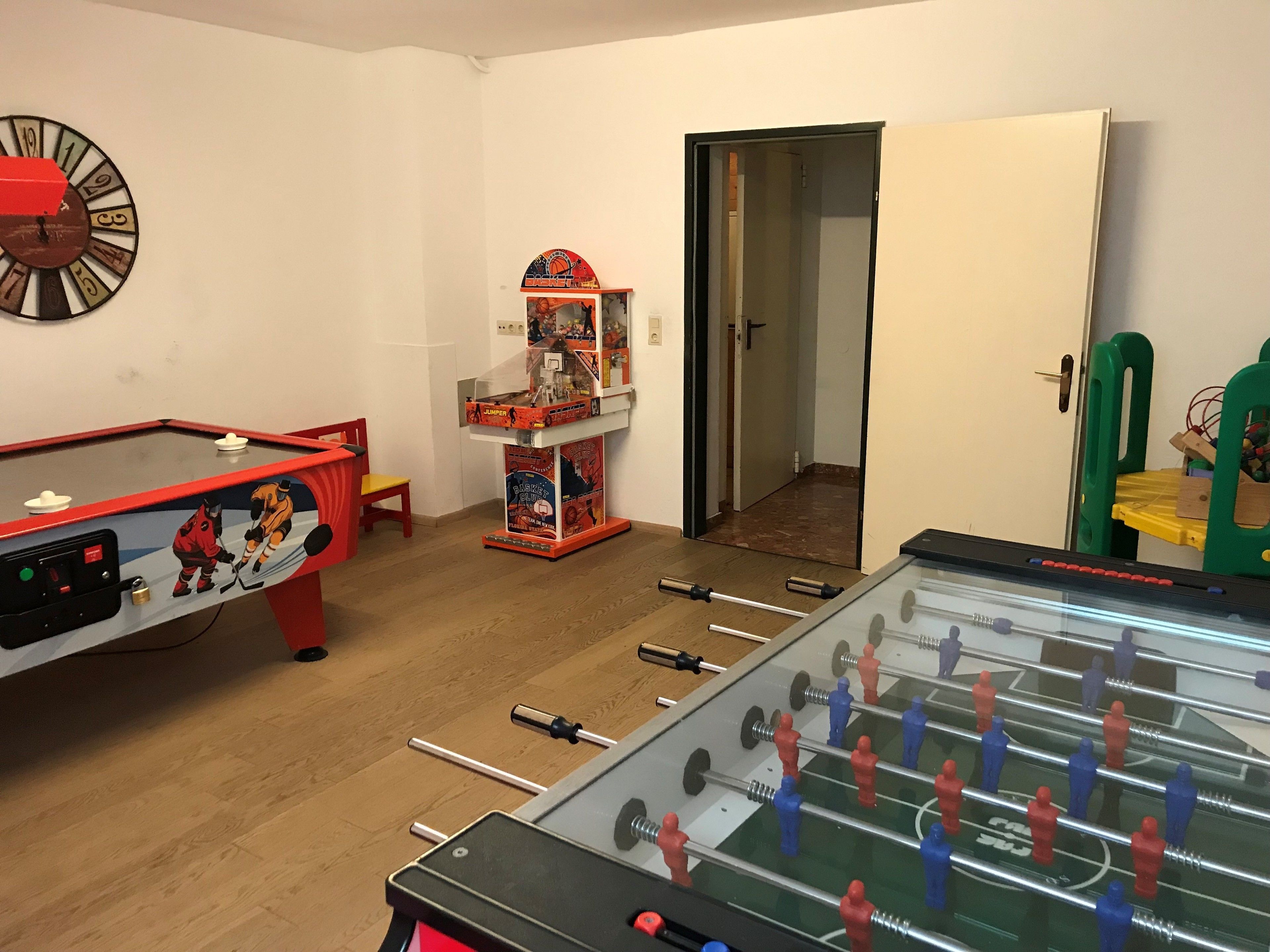 A room with a foosball table, a pool table, and a dartboard.