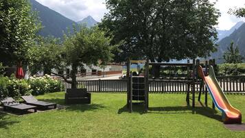 Un parque infantil con tobogán, estructuras para escalar y bancos, con una montaña al fondo.