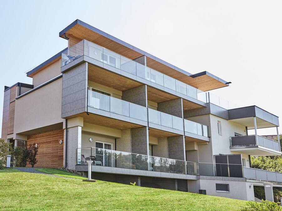 A modern multi-story residential building with balconies, large windows, and a flat roof.
