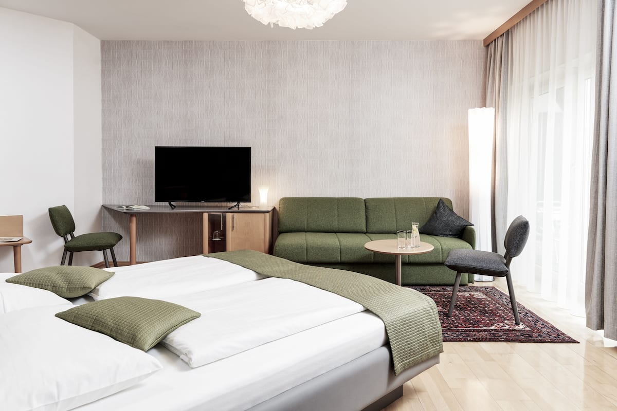 A hotel room with a bed, a green sofa, a small table, a TV, and a desk.