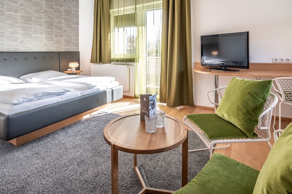 A modern hotel room with a bed, a television, a small table with glasses, and a green chair.