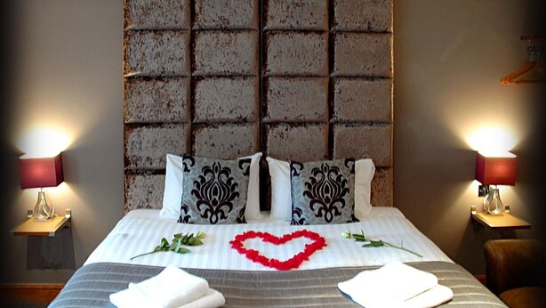 A hotel room with a large bed, a decorative heart on the bed, and two bedside lamps. - Homestay Hotel (Hounslow)