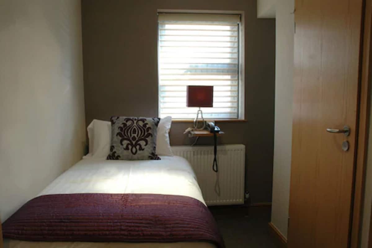 A bedroom with a bed, a radiator, a window with blinds, and a door.