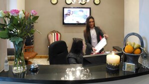 A reception area with a TV, a vase of flowers, a candle, and a fruit basket. - Homestay Hotel (Hounslow)
