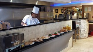 A chef preparing food in a modern kitchen with a buffet setup. - Homestay Hotel (Hounslow)