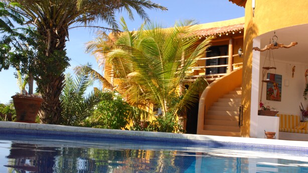 A swimming pool with a clear view of the surrounding architecture, including a building with a tiled roof and a staircase leading to an upper level. - Stevie WonderLand (Díaz)