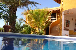A swimming pool with a clear view of the surrounding architecture, including a building with a tiled roof and a staircase leading to an upper level. - Stevie WonderLand (Díaz)