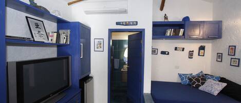 A compact room with a TV, blue furniture, and a door leading to another area.