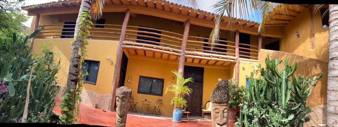 A yellow building with a balcony, surrounded by cacti and plants.