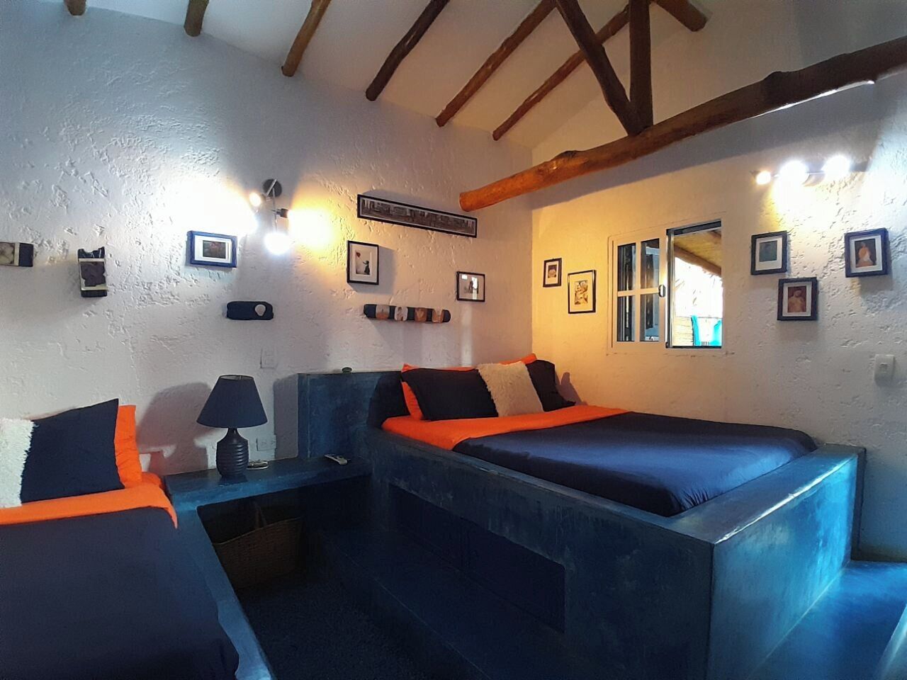 Una habitación con dos camas, una mesita de noche, una lámpara y cuadros en las paredes.