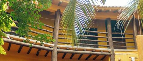 Un edificio amarillo con una escalera de madera que lleva a una puerta, dos esculturas de piedra y una palmera.