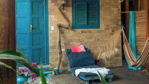 A rustic room with a wooden ceiling, a hammock, a bed with blue bedding, and a blue door. - Stevie WonderLand (Díaz)