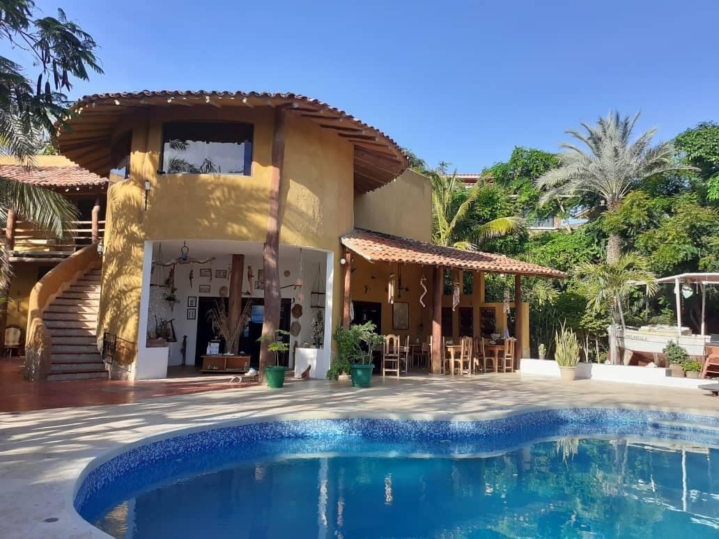 Zona de piscina con una piscina azul cristalina, un porche cubierto con asientos exteriores y una escalera que lleva a un nivel superior.