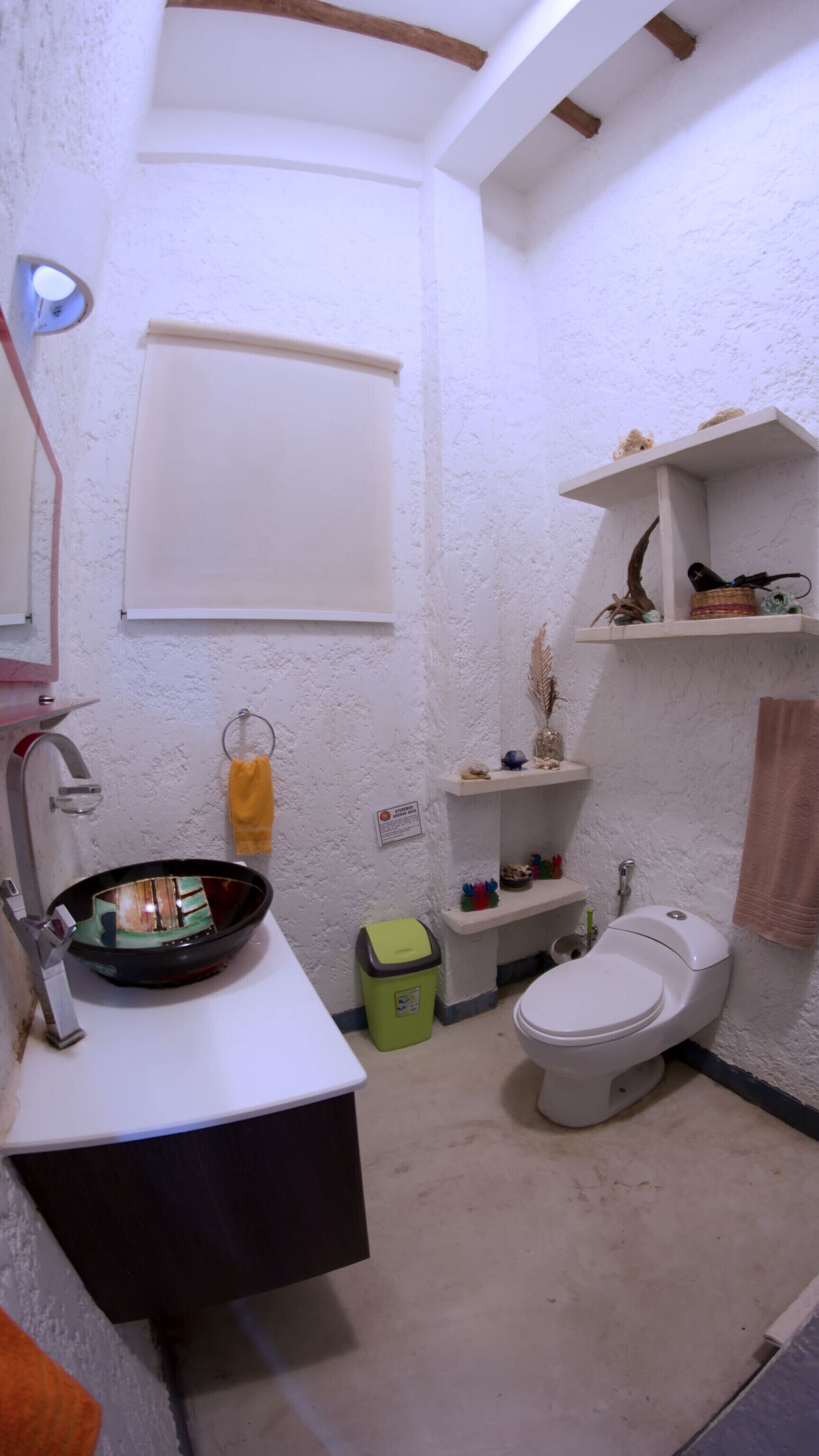 A compact bathroom with a white sink, a toilet, and a small shelf with toiletries.