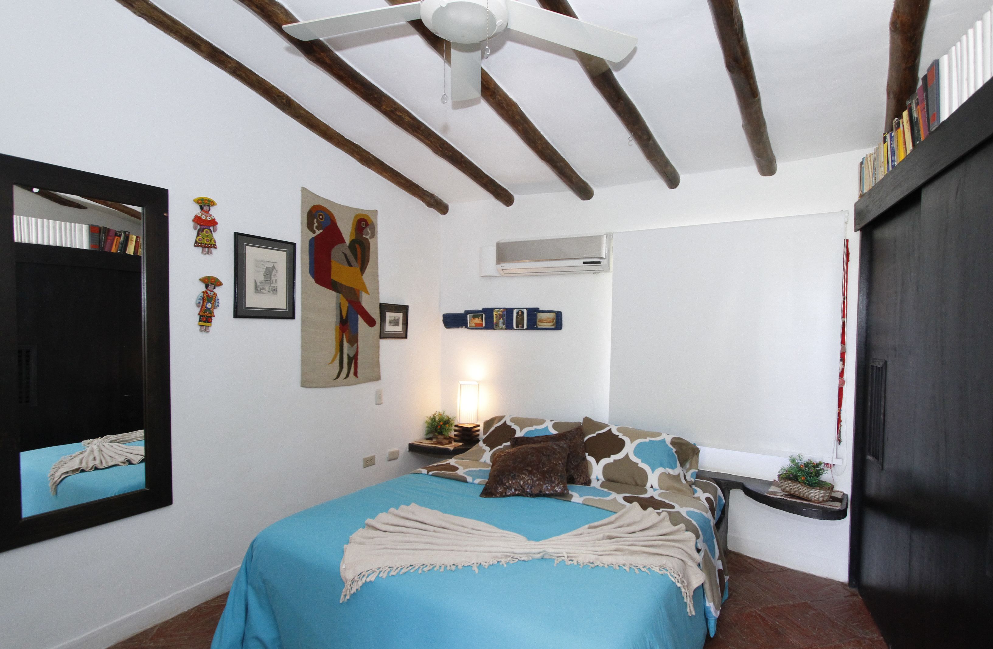 A bedroom with a bed, a ceiling fan, a wall-mounted air conditioner, and a bookshelf.