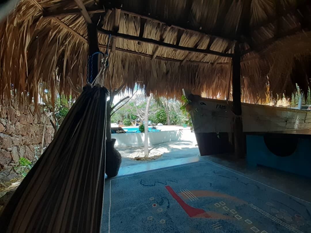 Een kamer met rieten dak, een hangmat en uitzicht op een buitenzwembad.